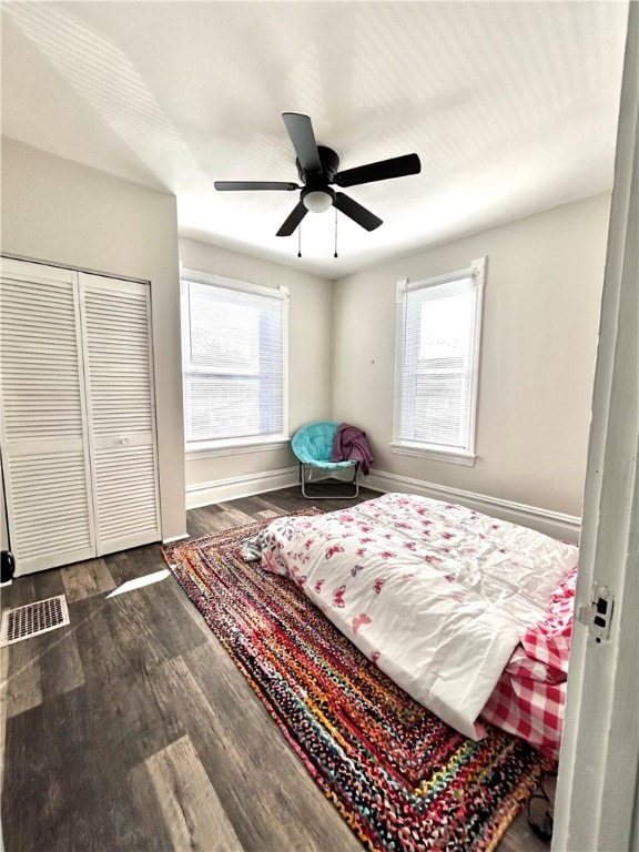 bedroom featuring dark wood-type flooring, multiple windows, a closet, and ceiling fan