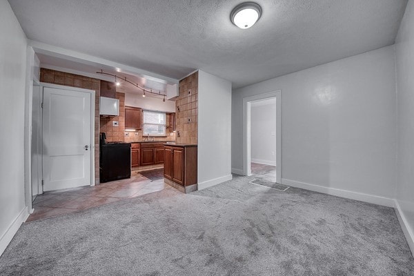 kitchen with tasteful backsplash, black range oven, light colored carpet, and a textured ceiling