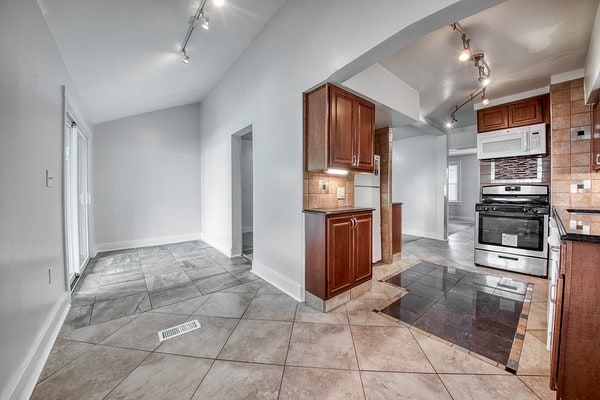 kitchen featuring lofted ceiling, rail lighting, refrigerator, stainless steel range, and decorative backsplash