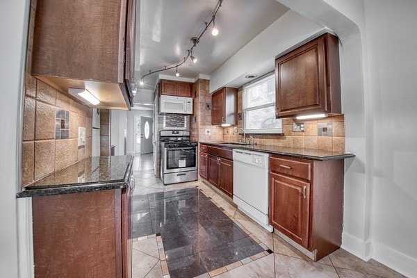 kitchen with decorative backsplash, white appliances, sink, and dark stone counters