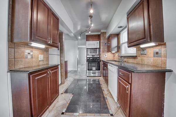 kitchen featuring rail lighting, white appliances, sink, decorative backsplash, and light tile patterned floors