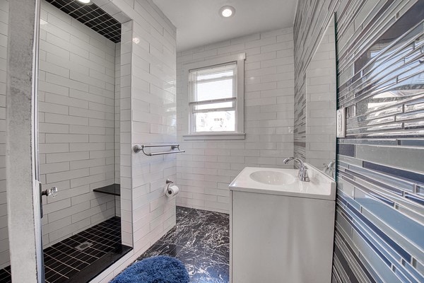 bathroom with tiled shower, vanity, and tile walls