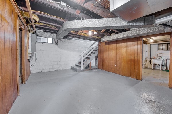 basement with wood walls, electric panel, and sink