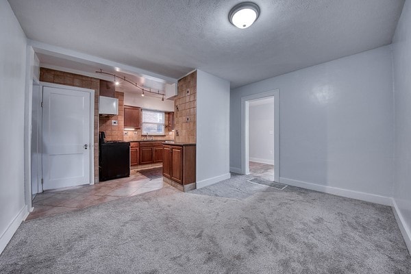 kitchen featuring a textured ceiling, light carpet, tasteful backsplash, and black range oven