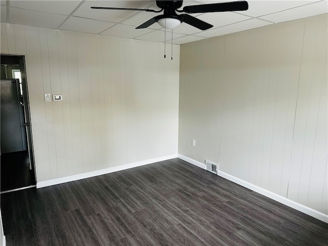 unfurnished room with dark hardwood / wood-style flooring, a paneled ceiling, wooden walls, and ceiling fan