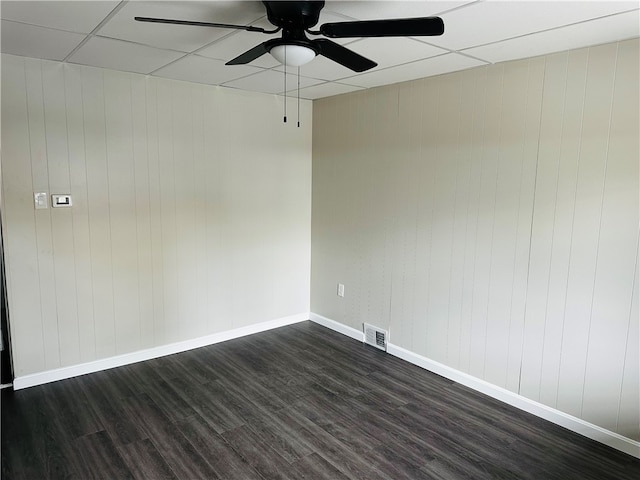 spare room featuring wood walls, ceiling fan, dark hardwood / wood-style flooring, and a drop ceiling