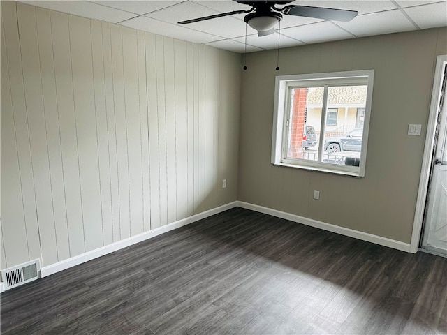 empty room featuring wood walls, dark hardwood / wood-style flooring, a paneled ceiling, and ceiling fan