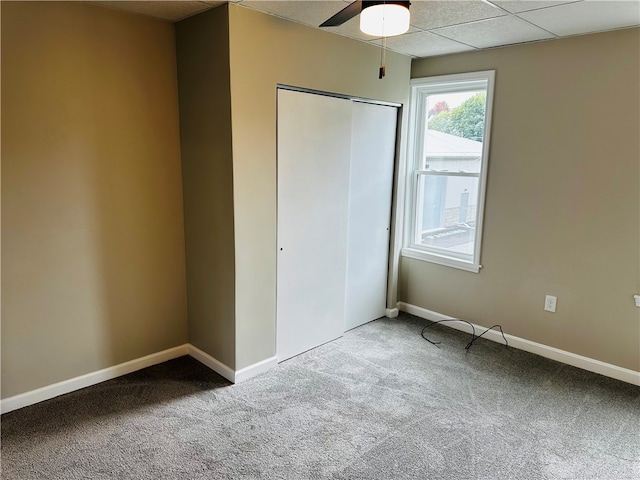 unfurnished bedroom with a closet, a drop ceiling, carpet flooring, and ceiling fan