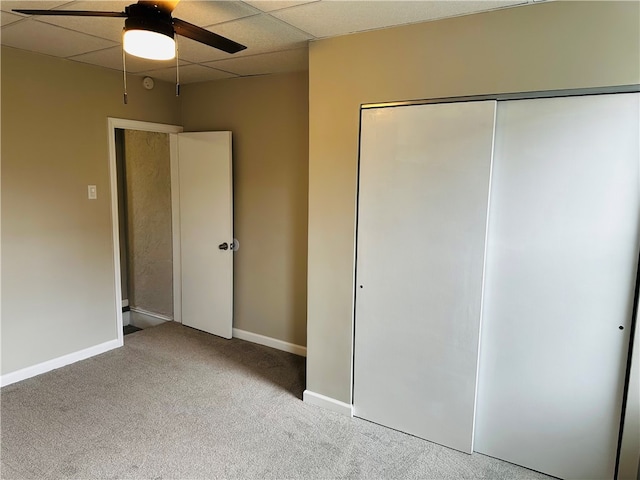 unfurnished bedroom with a drop ceiling, ceiling fan, a closet, and light colored carpet