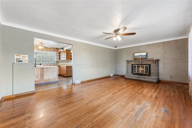 unfurnished living room with wood-type flooring, a brick fireplace, and ceiling fan