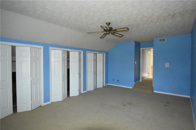 unfurnished bedroom featuring ceiling fan, dark carpet, lofted ceiling, two closets, and a textured ceiling