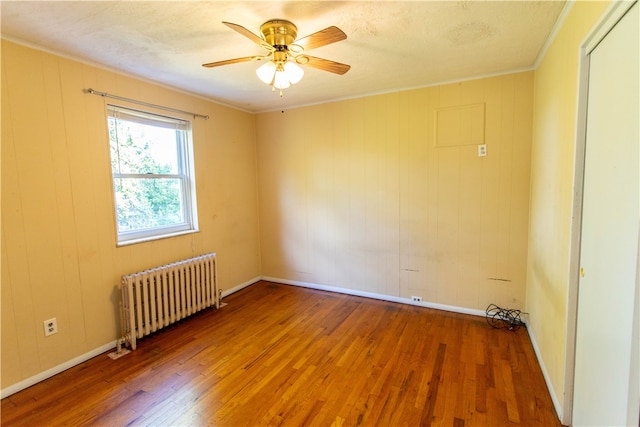 empty room featuring ceiling fan, radiator heating unit, crown molding, hardwood / wood-style floors, and wooden walls