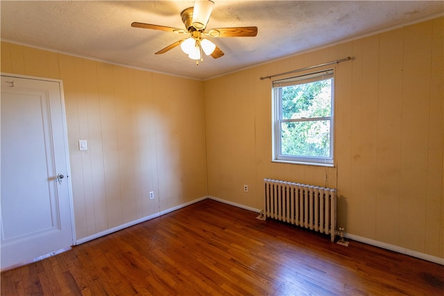 spare room with wood walls, ceiling fan, radiator heating unit, crown molding, and hardwood / wood-style flooring