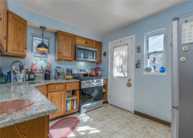 kitchen with sink, hanging light fixtures, light stone counters, backsplash, and appliances with stainless steel finishes