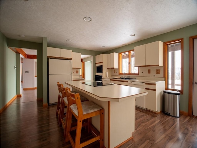 kitchen with dark wood finished floors, light countertops, a sink, white appliances, and a kitchen breakfast bar