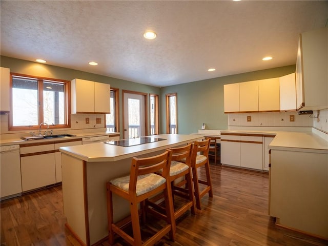 kitchen with tasteful backsplash, dark wood-type flooring, a sink, dishwasher, and black electric cooktop