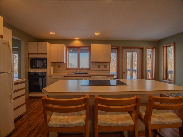 kitchen with dark wood-style flooring, light countertops, white cabinets, a sink, and black appliances