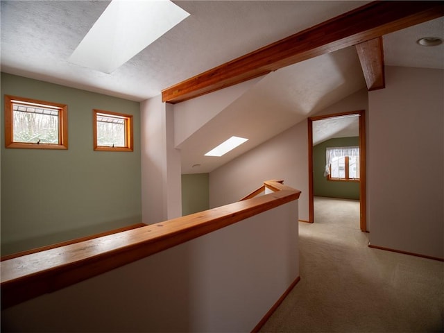 corridor featuring light carpet, vaulted ceiling with skylight, a textured ceiling, and an upstairs landing