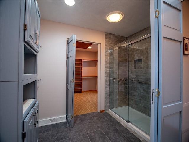 bathroom featuring a shower stall, a spacious closet, baseboards, and tile patterned flooring