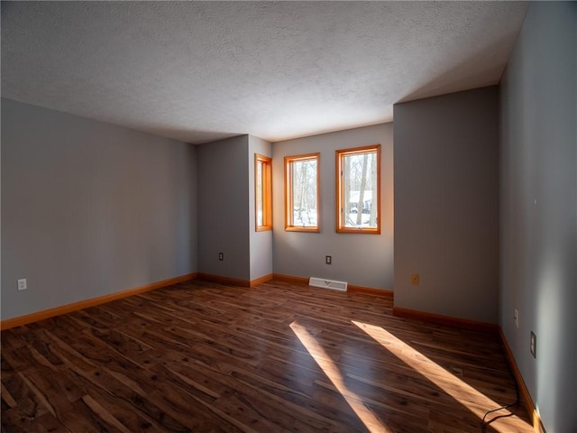 unfurnished room with visible vents, a textured ceiling, baseboards, and wood finished floors