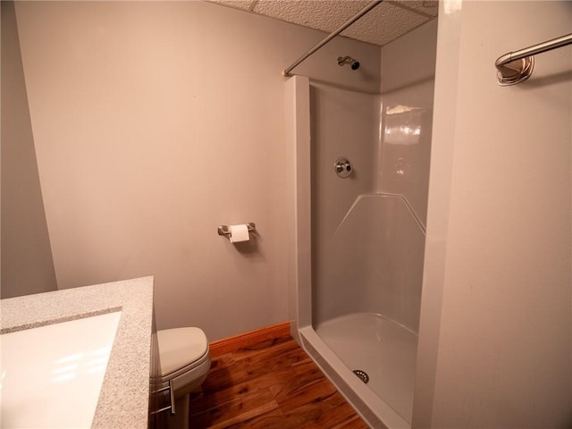 bathroom featuring toilet, vanity, wood finished floors, baseboards, and a walk in shower