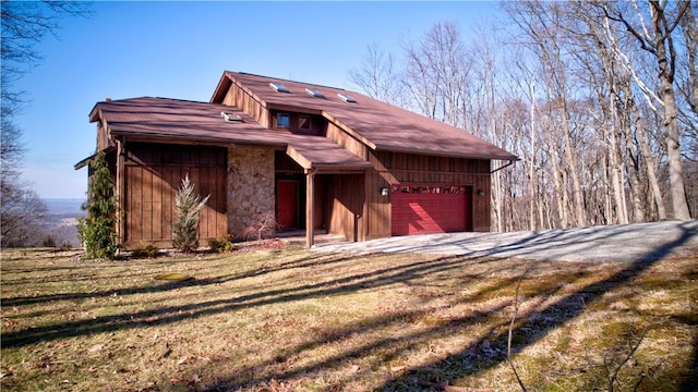 view of front facade featuring a garage, a front yard, stone siding, and driveway