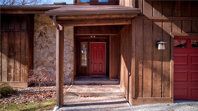 view of exterior entry with a garage, stone siding, and board and batten siding