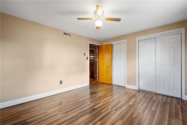 unfurnished bedroom with hardwood / wood-style flooring, ceiling fan, and multiple closets