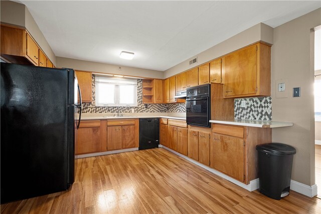 kitchen with tasteful backsplash, sink, black appliances, and light wood-type flooring