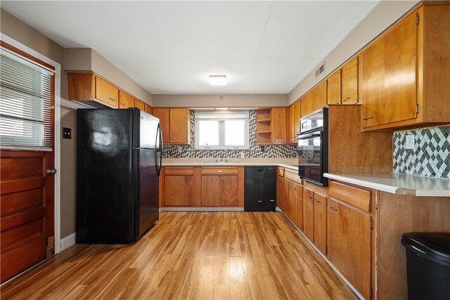 kitchen with tasteful backsplash, light hardwood / wood-style flooring, black appliances, and sink