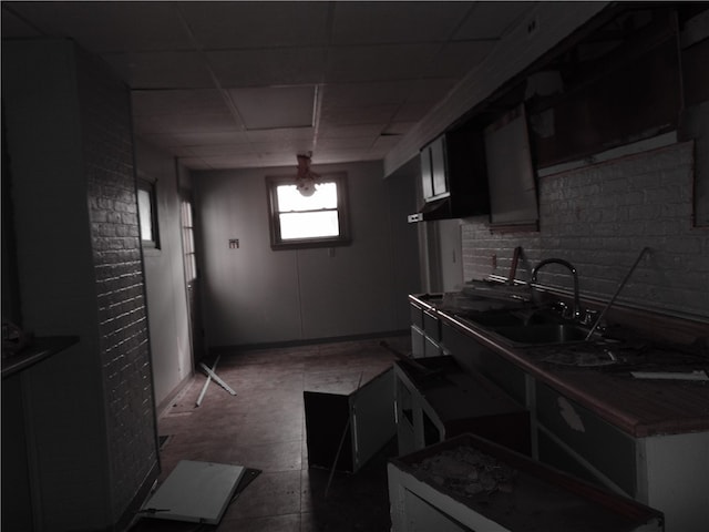 kitchen featuring a drop ceiling, brick wall, and sink