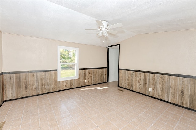 unfurnished room featuring ceiling fan, a textured ceiling, lofted ceiling, and wooden walls