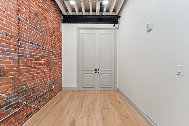 spare room featuring brick wall and light hardwood / wood-style flooring