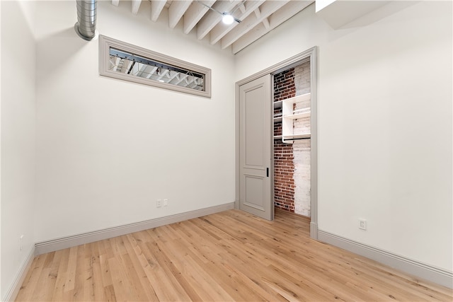 spare room with beam ceiling and light hardwood / wood-style flooring