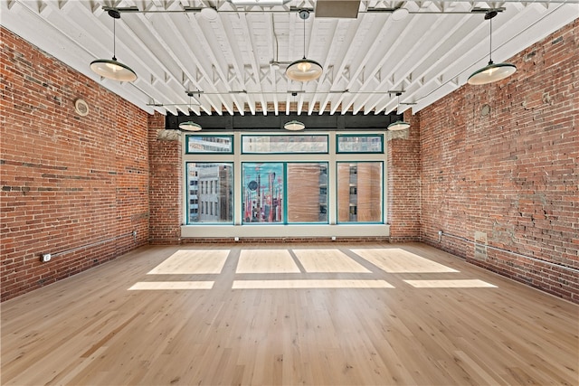 empty room with brick wall, hardwood / wood-style flooring, and track lighting