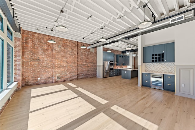 interior space with beverage cooler, a towering ceiling, light hardwood / wood-style floors, and brick wall