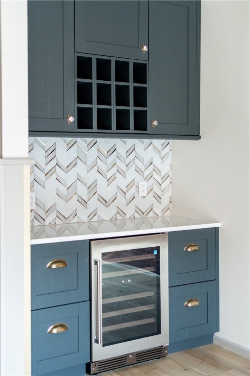 bar featuring light wood-type flooring, wine cooler, and blue cabinets