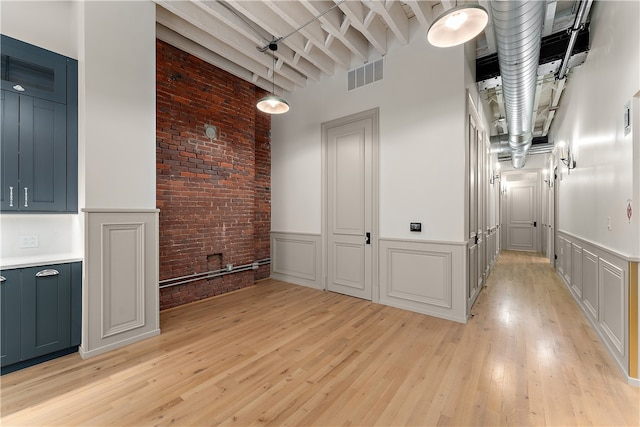 interior space with brick wall, beamed ceiling, light wood-type flooring, and a towering ceiling