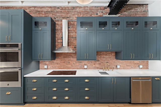 kitchen with double oven, wall chimney exhaust hood, sink, brick wall, and black electric stovetop