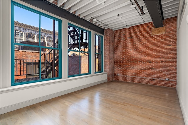 empty room with hardwood / wood-style flooring, beamed ceiling, and brick wall