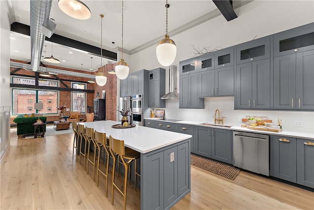 kitchen featuring a kitchen island, stainless steel appliances, a breakfast bar, sink, and wall chimney range hood