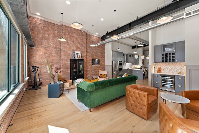 living room with a high ceiling, wine cooler, brick wall, and light hardwood / wood-style flooring