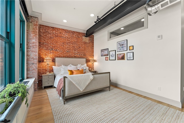 bedroom featuring beam ceiling, brick wall, and light hardwood / wood-style flooring