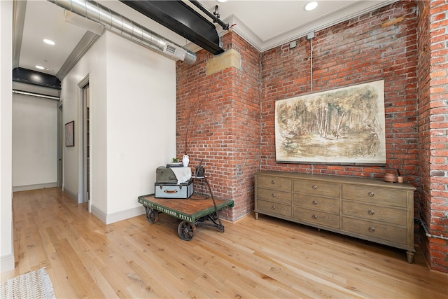 living area with crown molding, light hardwood / wood-style flooring, and brick wall