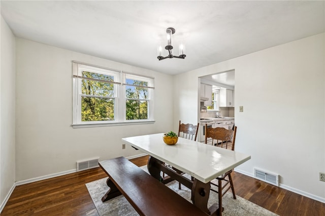 dining area with sink, dark wood-type flooring, and an inviting chandelier