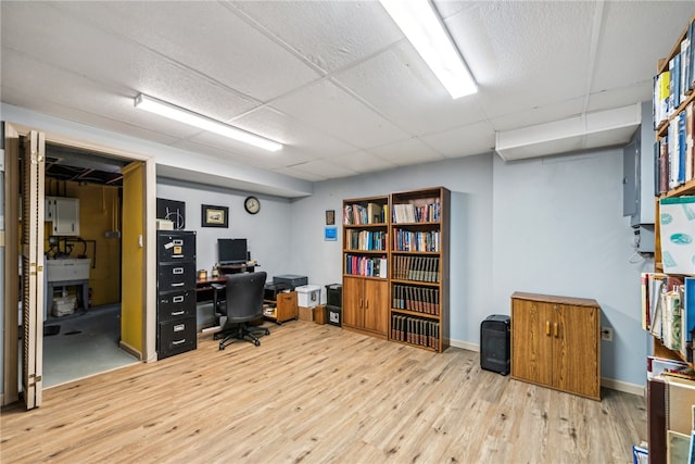 home office featuring a drop ceiling, electric panel, and light hardwood / wood-style flooring