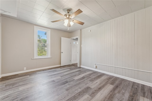 unfurnished room with light hardwood / wood-style floors, wooden walls, and ceiling fan