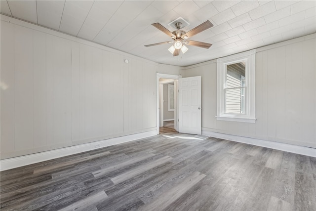 empty room with ceiling fan, wood walls, and wood-type flooring