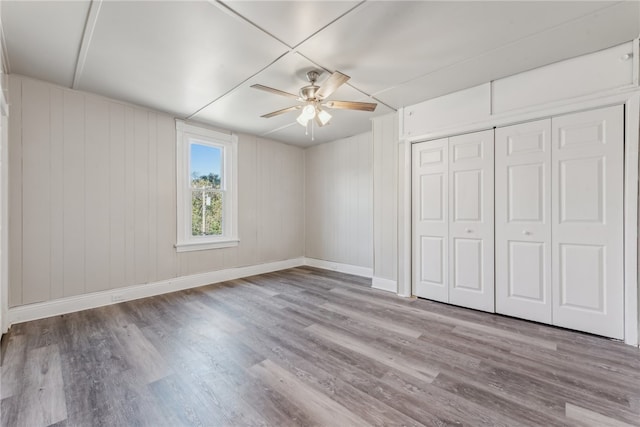 unfurnished bedroom featuring ceiling fan, light hardwood / wood-style flooring, wood walls, and a closet