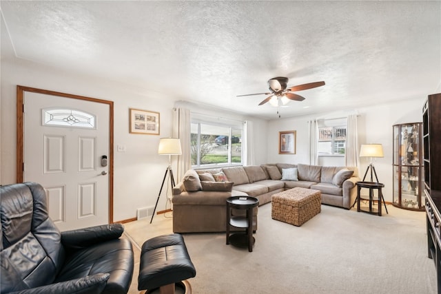 living room with ceiling fan, light carpet, and a textured ceiling